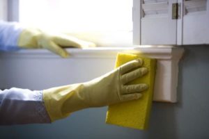 person wearing protective gloves wipes the window sill with a sponge