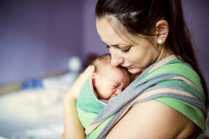 Newborn baby hold by mother in the baby wrap carrier.