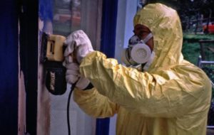 man wearing a protective suit and respirator while sanding off paint
