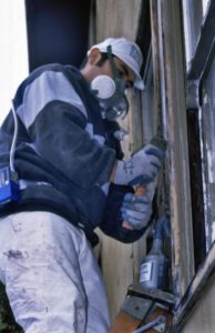 worker wears respirator and protective gloves while scraping paint off the windowsill